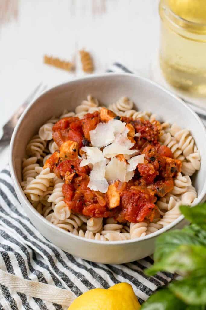 Chicken Arrabbiata sauce over gluten-free rotini pasta with shaved parmesan on top.  Bowl on a striped towel.