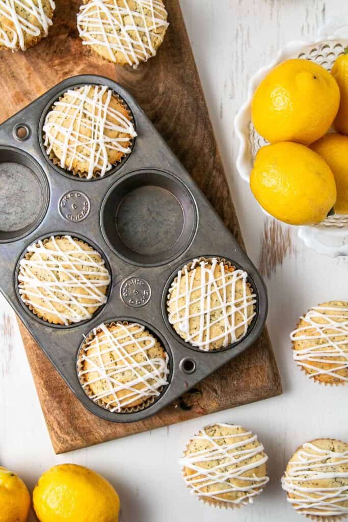 Gluten-free lemon poppy seed muffins in an old ecko muffin tin, on a wooden board, next to a bowl of lemons.