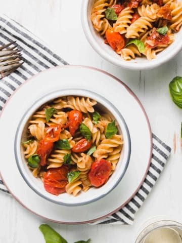 Burst tomato pasta in two enamel bowls. adorned with fresh torn basil.