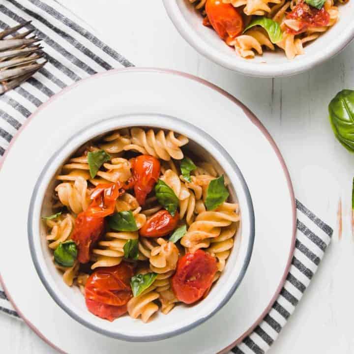 Burst tomato pasta in two enamel bowls. adorned with fresh torn basil.
