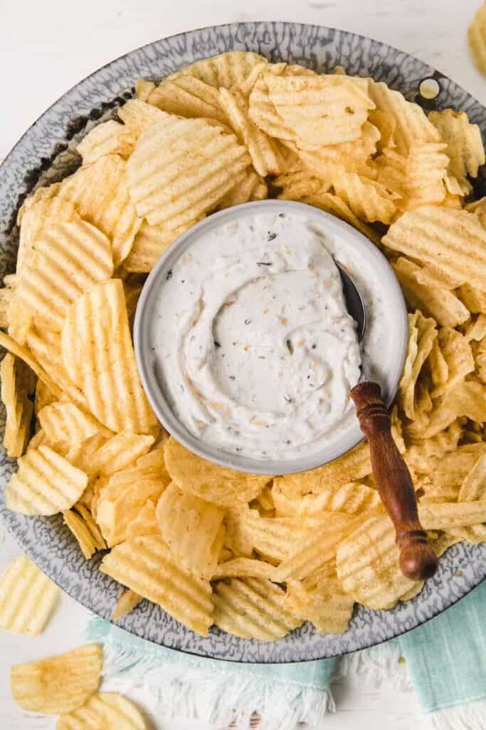 Gluten-free French onion chip dip in old enamelware bowl surrounded by wavy potato chips.
