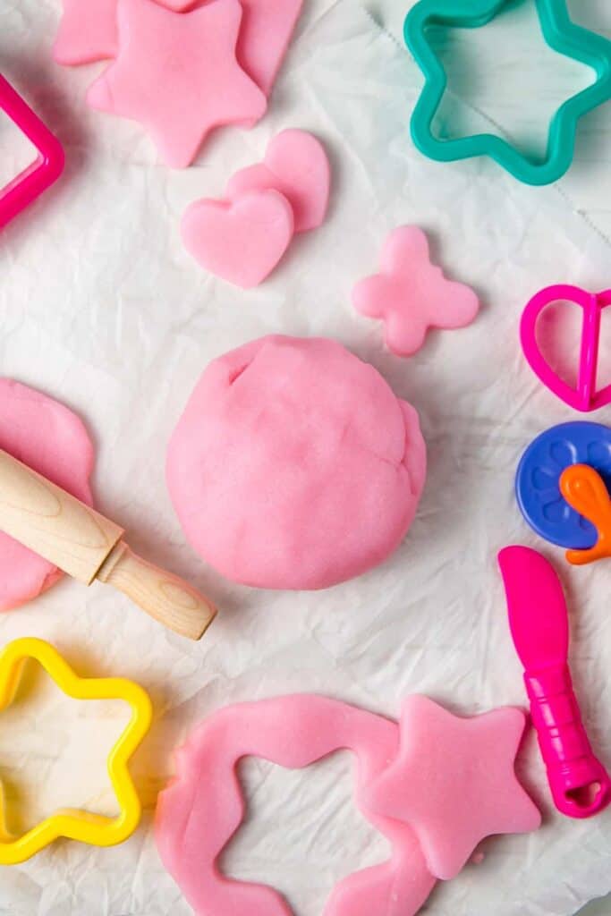 A ball of pink gluten-free play dough next to some play dough that is rolled out and cut into star, heart, and butterfly shapes.