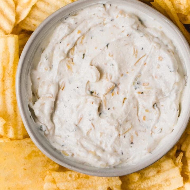 Gluten-free onion chip dip in a bowl next to wavy potato chips.