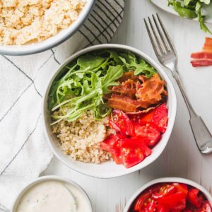 Quinoa, arugula, bacon, tomatoes, and yogurt dressing all laid out in bowls.