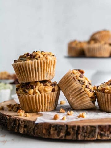 Gluten-free zucchini muffins with walnuts and chocolate chips strewn on a rustic wood platter.