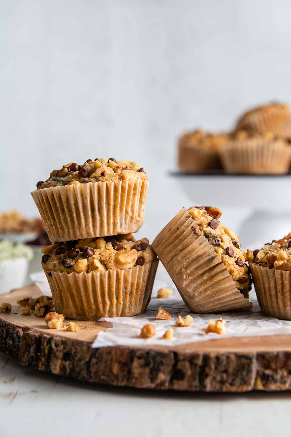 Gluten-free zucchini muffins with walnuts and chocolate chips strewn on a rustic wood platter.