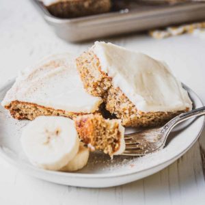 Gluten-free Frosted Banana Bars piled on a plate. A bite on a fork next to slice bananas.