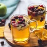 Mulled apple cider in clear glass mugs garnished with cranberries and apples.