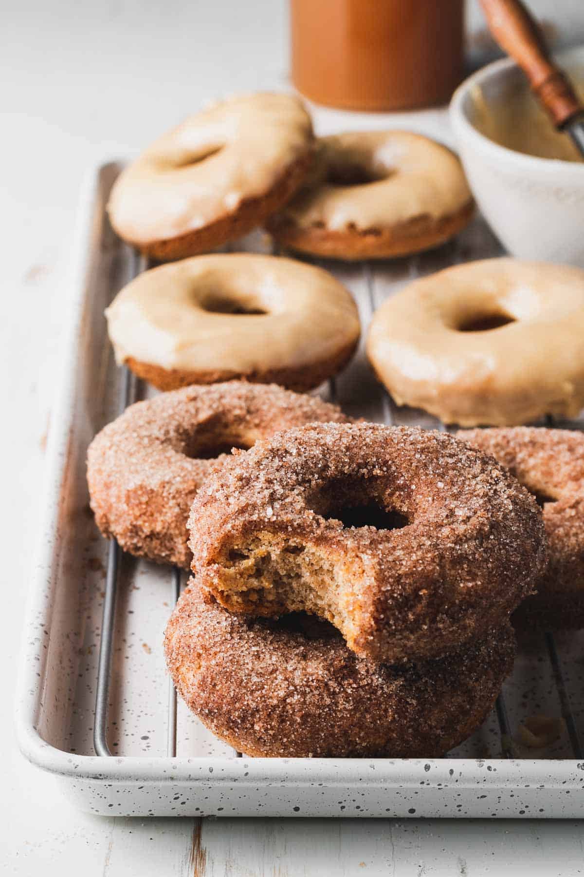 Apple cider donuts on a baking sheet already coated in cinnamon sugar and maple glaze.