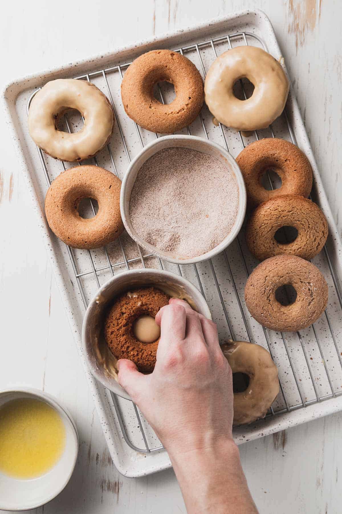 Dipping a donut in maple glaze. A bunch of donuts on a baking pan.