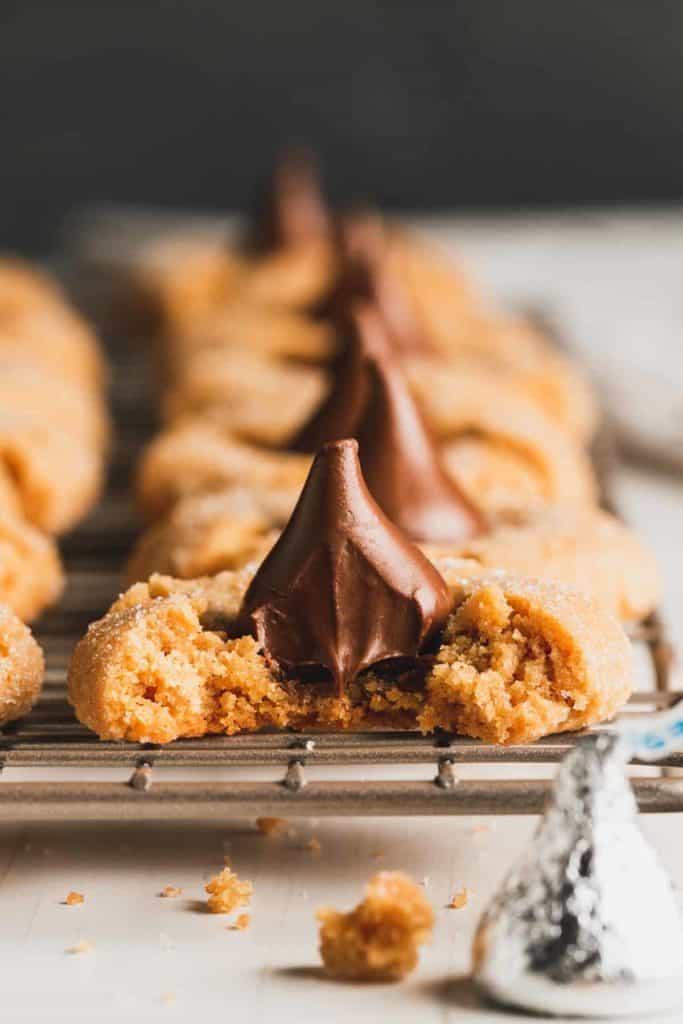 Flourless peanut butter blossoms with melty chocolate, one with a bite taken, on a wire rack.