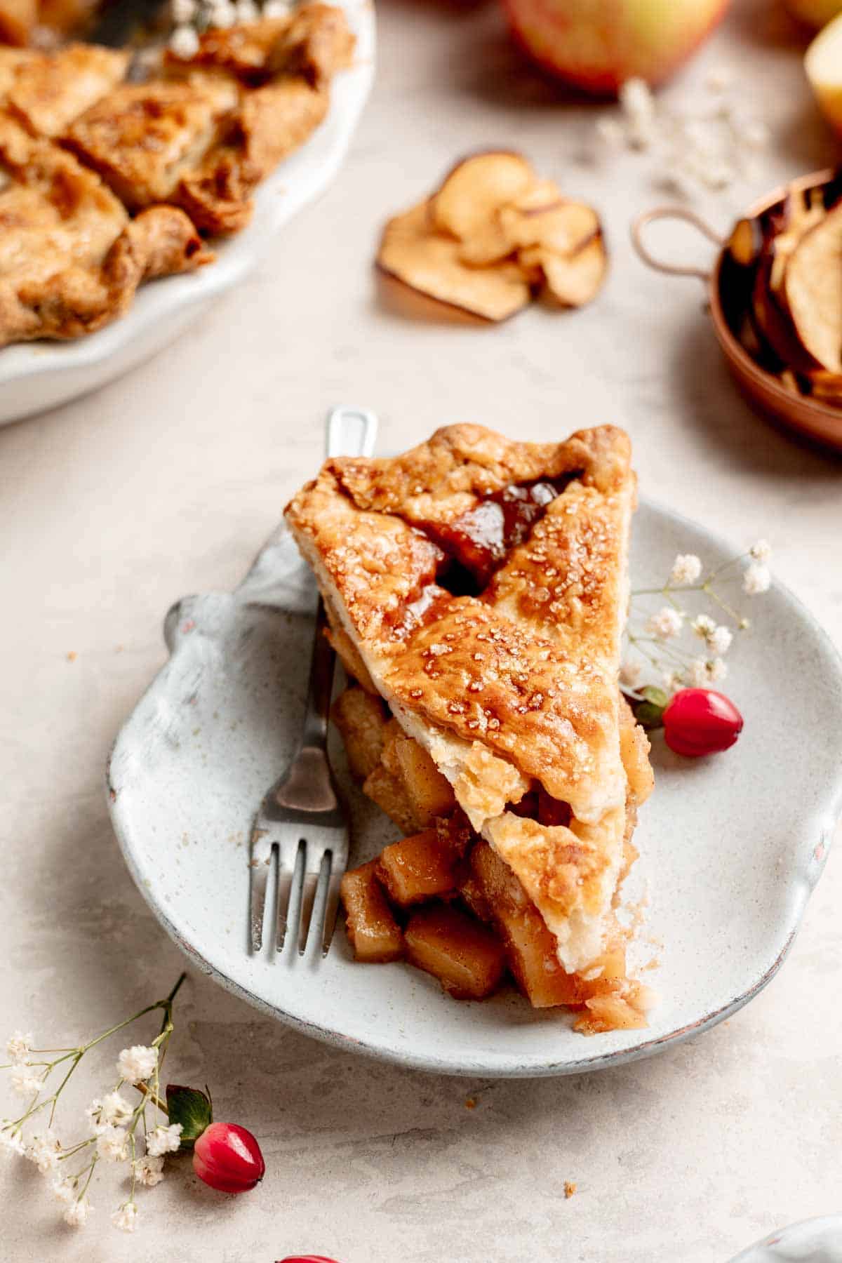 A slice of gluten free apple pie on a small apple shaped plate, apple filling spilling out the side.