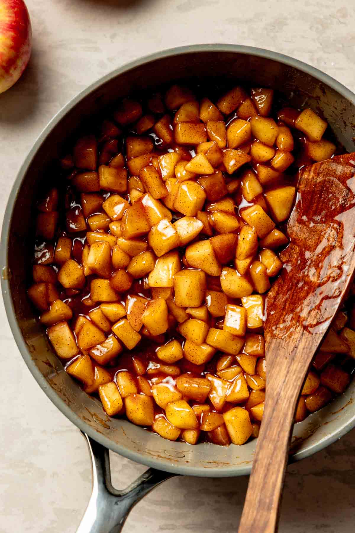 Apple pie filling in large skillet with wooden spoon resting to the side.