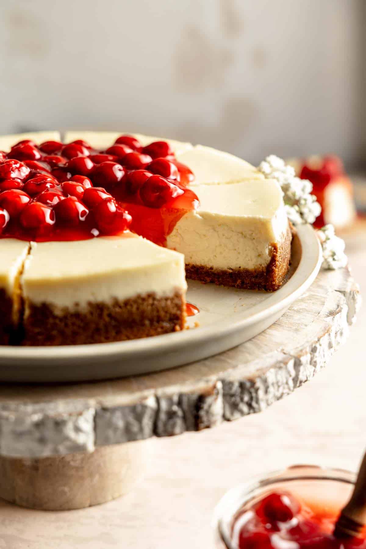 Gluten free cheesecake topped with cherry filling on a rustic wooden cake stand.