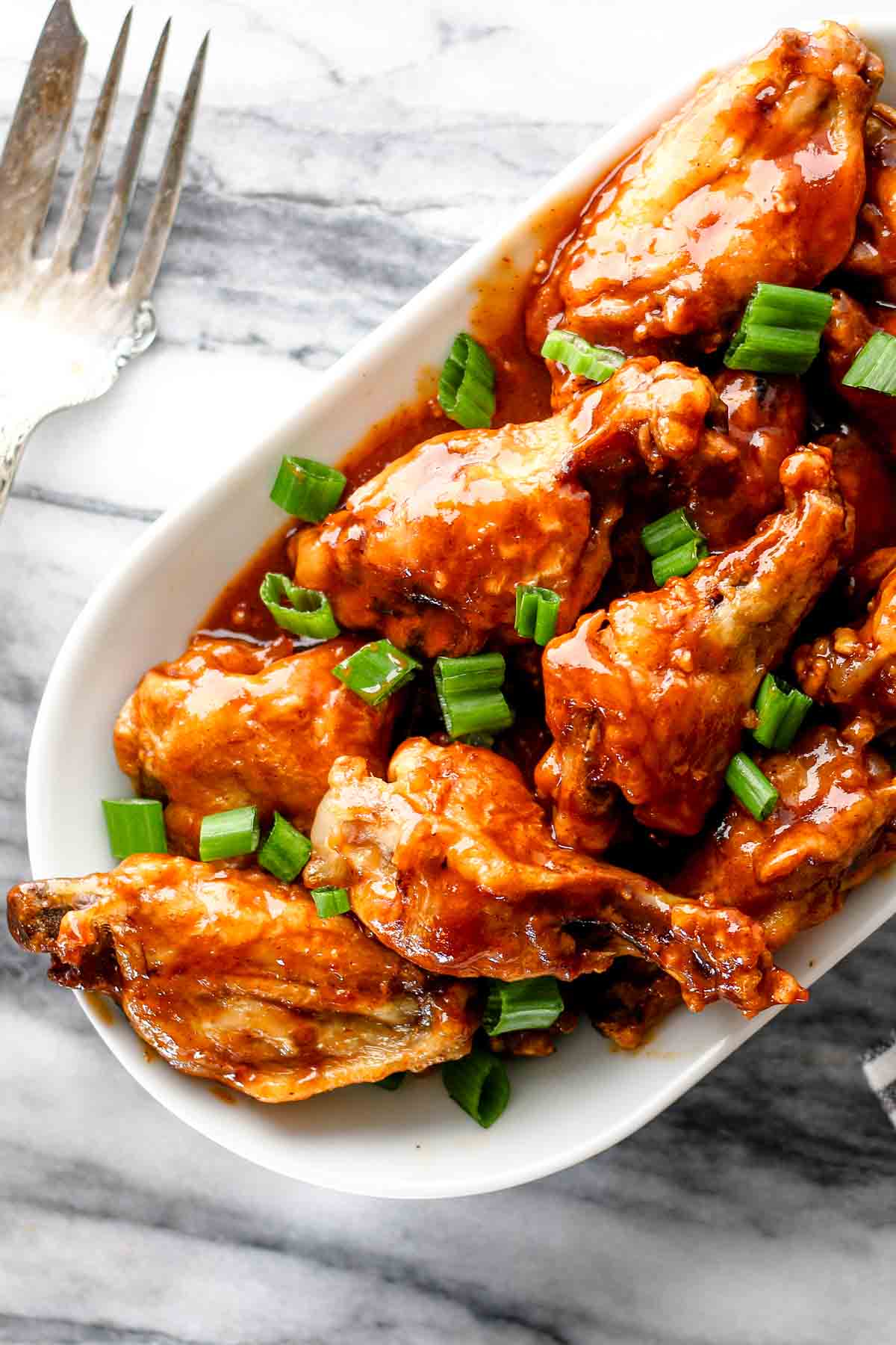 A platter of gluten free chicken wings in a barbecue sauce garnished with green onion.