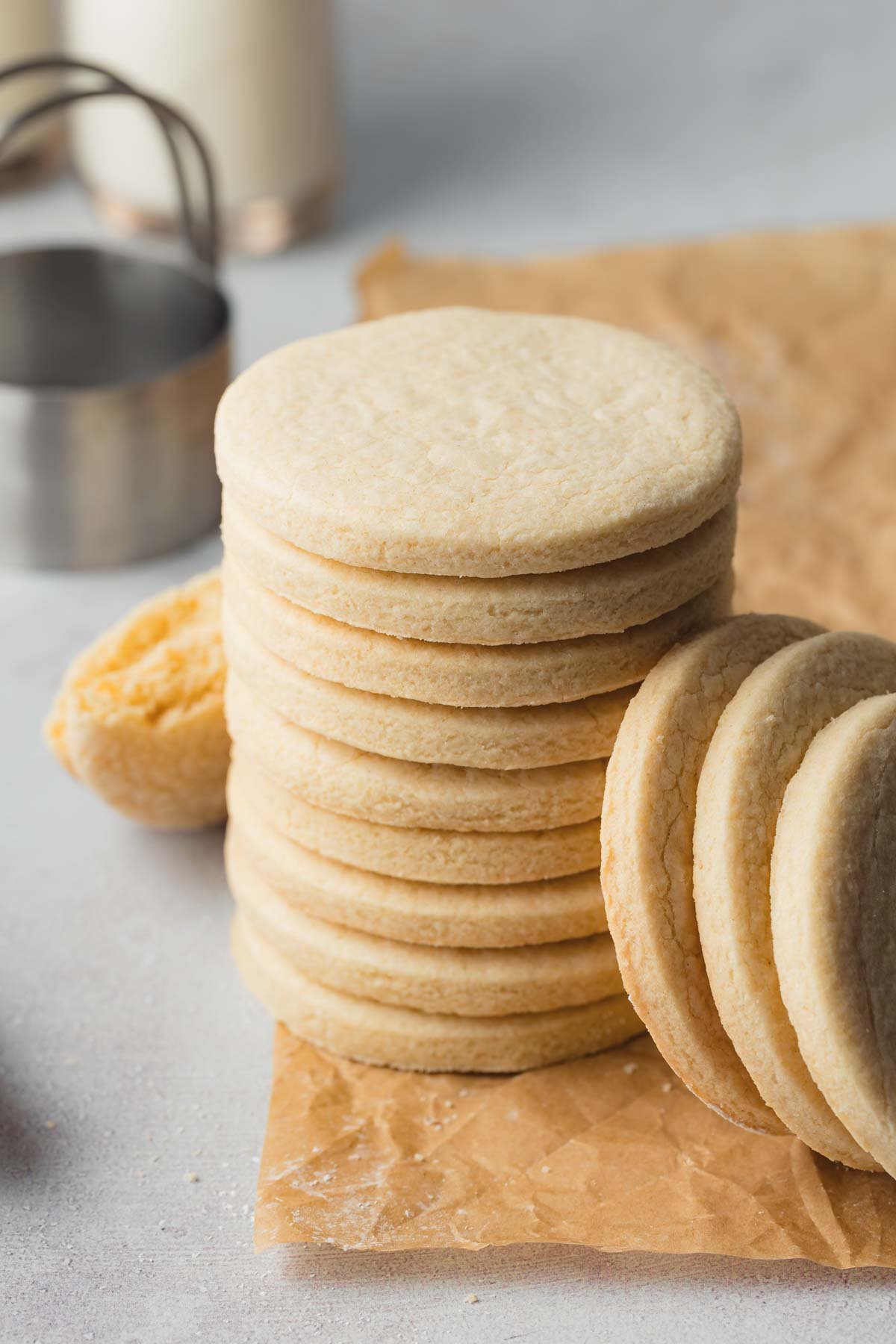 A stack of unfrosted, baked sugar cookie circles on a piece of parchment paper.