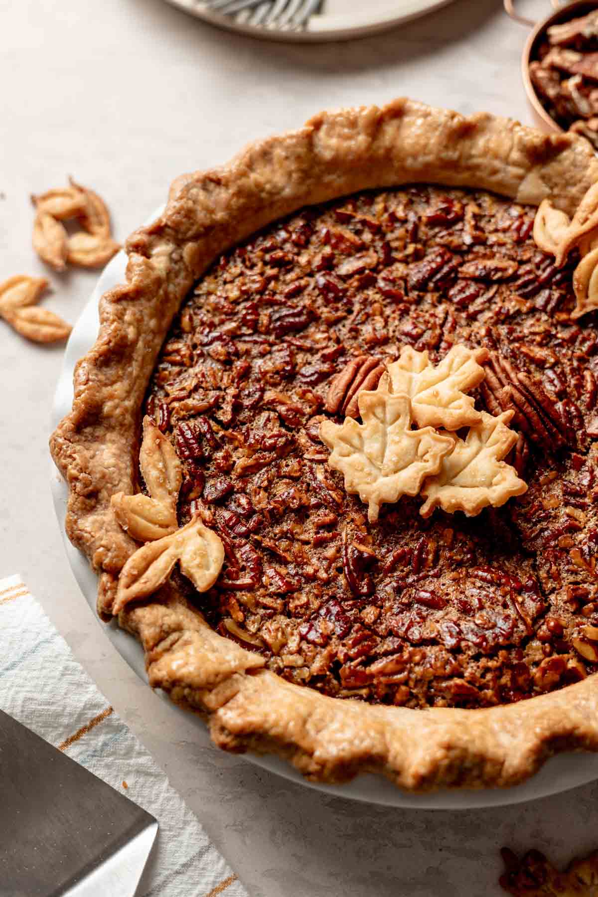 Whole gluten free pecan pie in golden brown pie crust with leave cutouts as garnish.