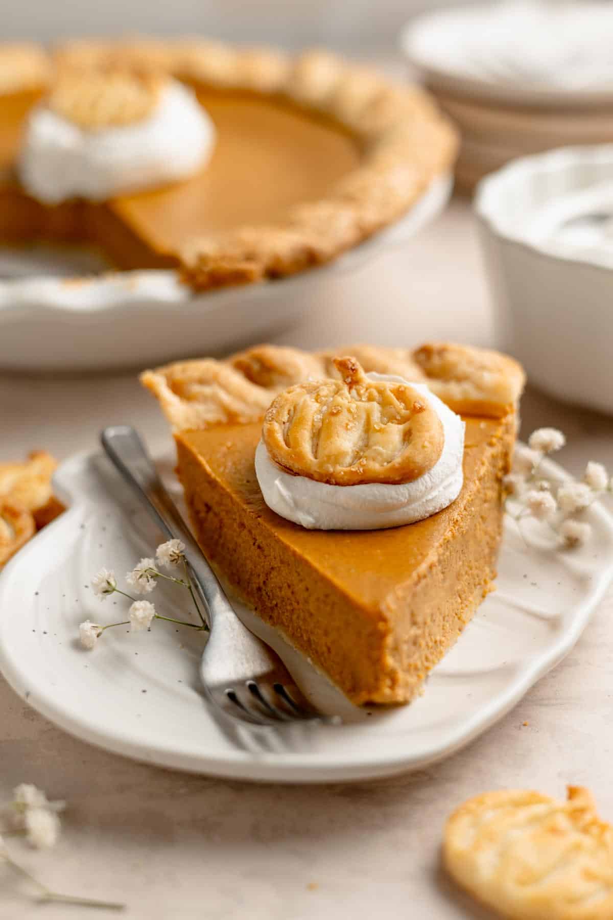 A perfect slice of gluten-free pumpkin pie garnished with whipped cream and a pumpkin-shaped crust cutout.