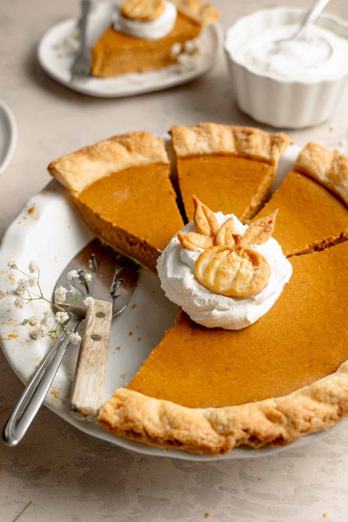 A sliced gluten free pumpkin pie with a dollop of cool whip and pumpkin shaped pie crust cutout. 