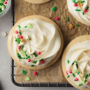 Gluten free sugar cookies on parchment lined rack, topped with frosting and sprinkles..