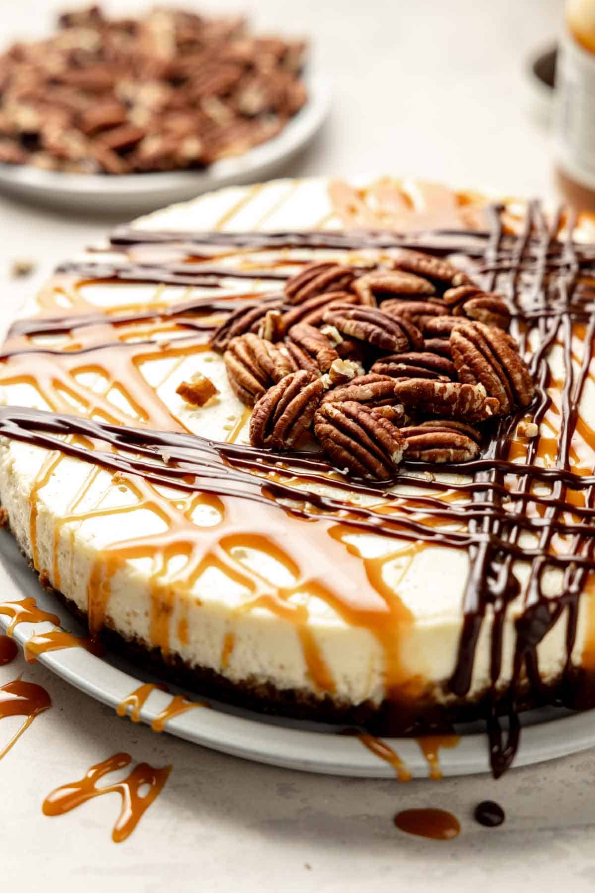 Gluten-free turtle cheesecake drizzled with caramel, fudge, and topped with pecans.