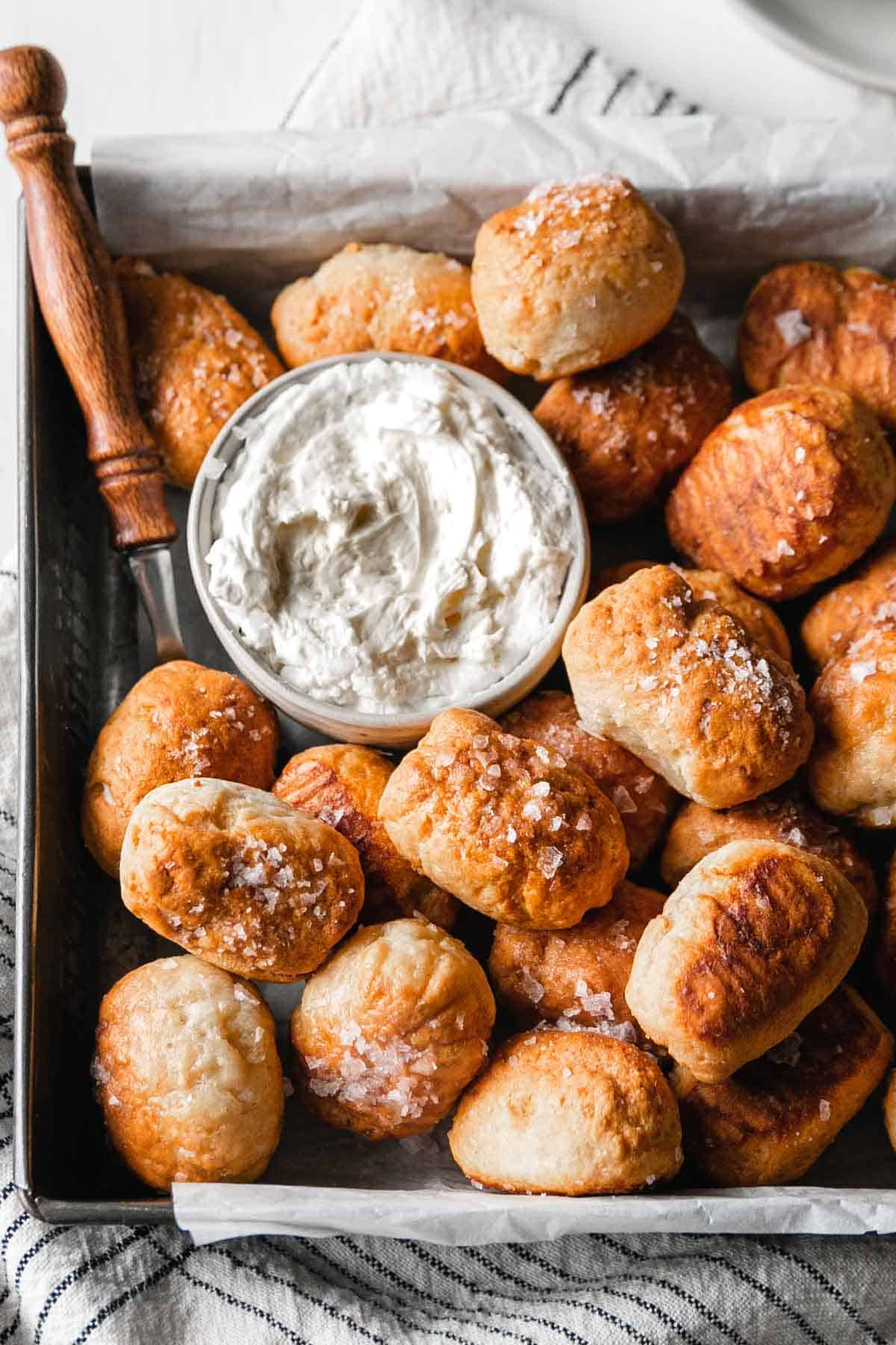 A tray full of gluten-free pretzel bites with a small bowl of cream cheese.