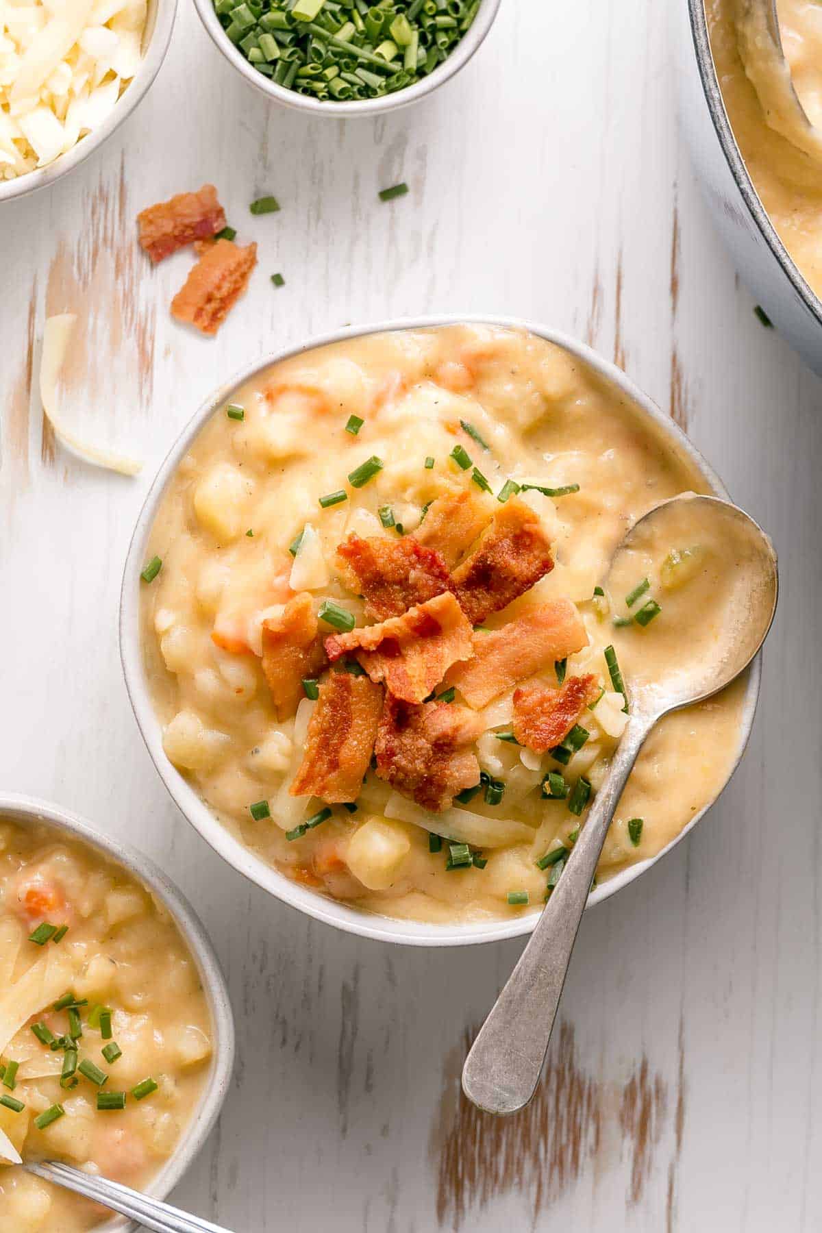 A bowl of creamy gluten-free potato soup topped with bacon, white cheddar cheese, and chives.