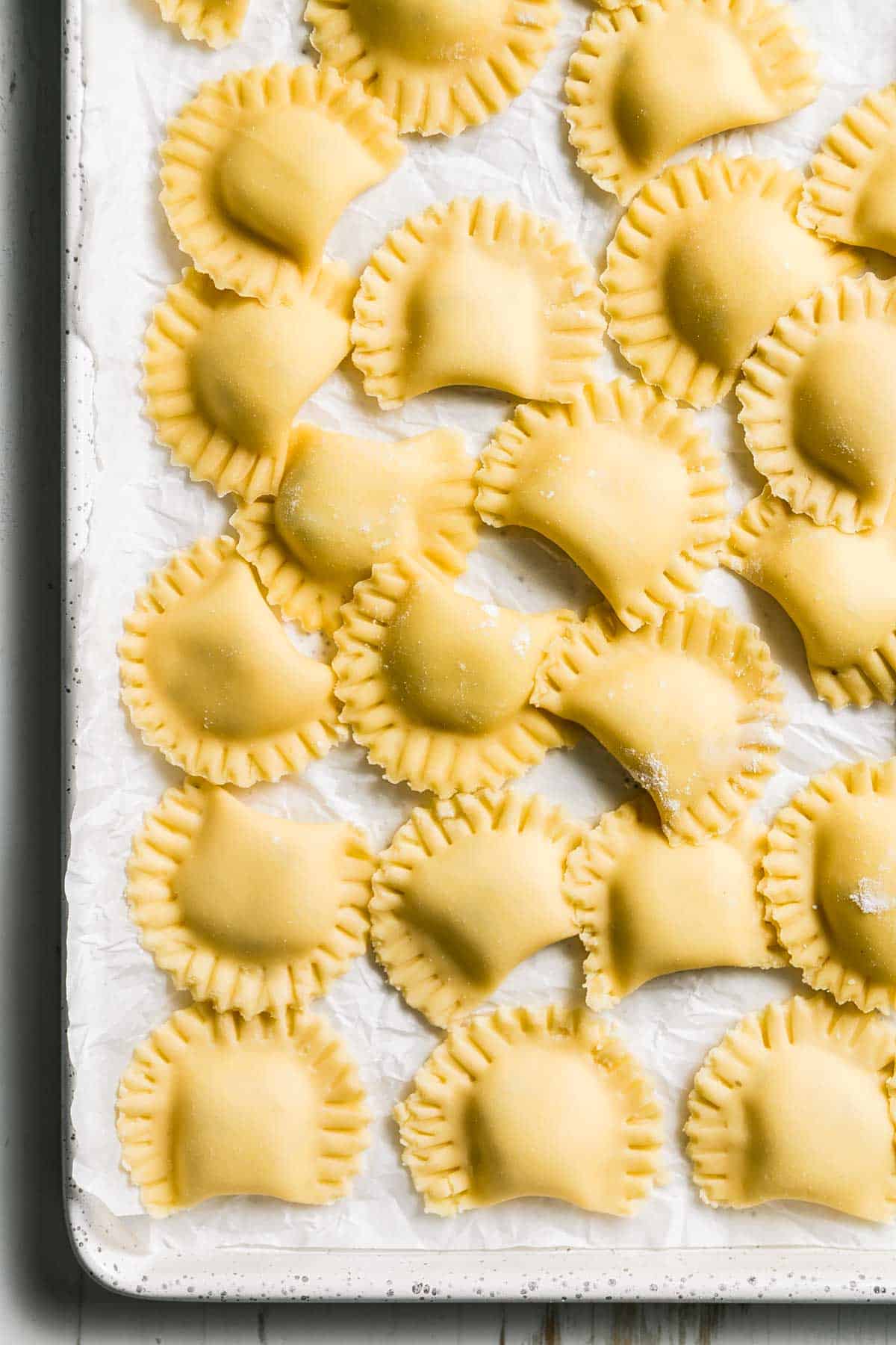 A baking pan full of gluten-free cheese ravioli in half moon shapes with crimped edges. 