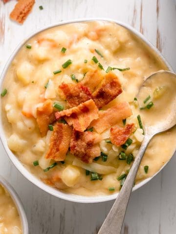 A bowl of creamy gluten-free potato soup topped with bacon, white cheddar cheese, and chives.