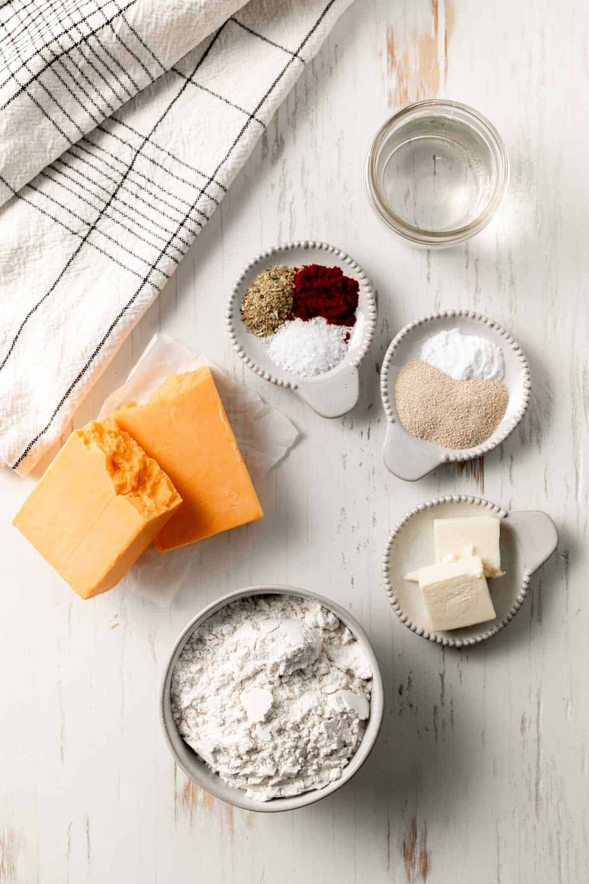 Ingredients for gluten-free cheese-it crackers measured out in bowls, a block of cheddar cheese broken in half.