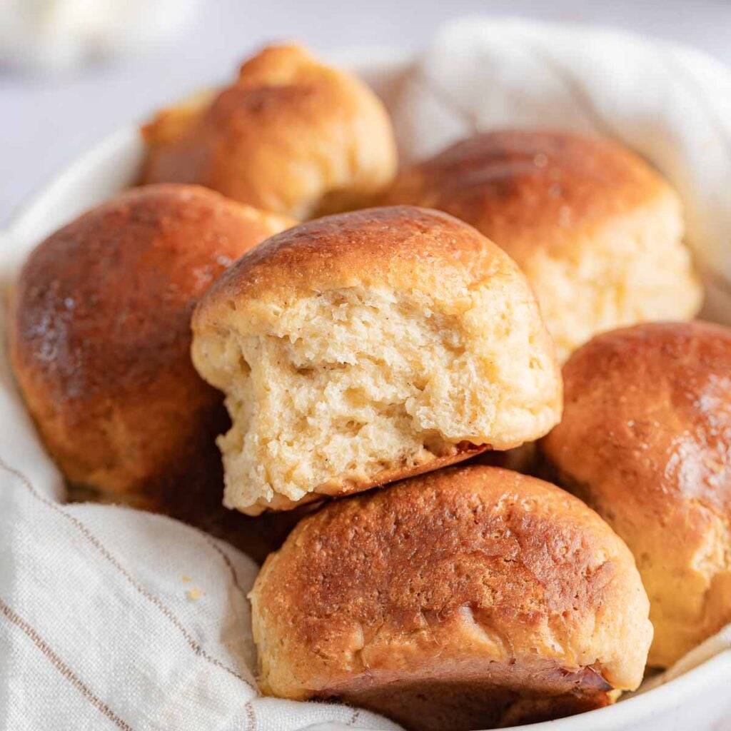 Gluten-Free Hawaiian Rolls stacked in a bowl with a linen towel.