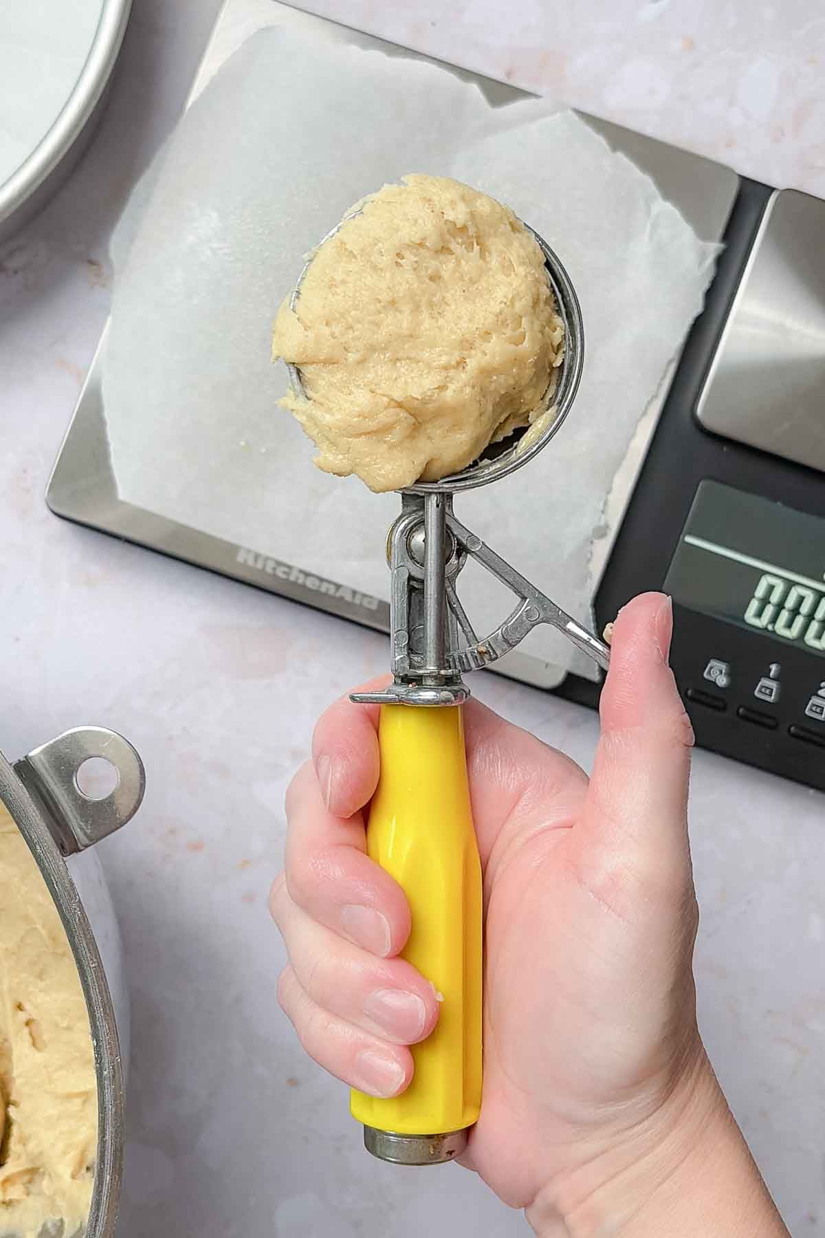Hand holding a portion scoop full of dough.