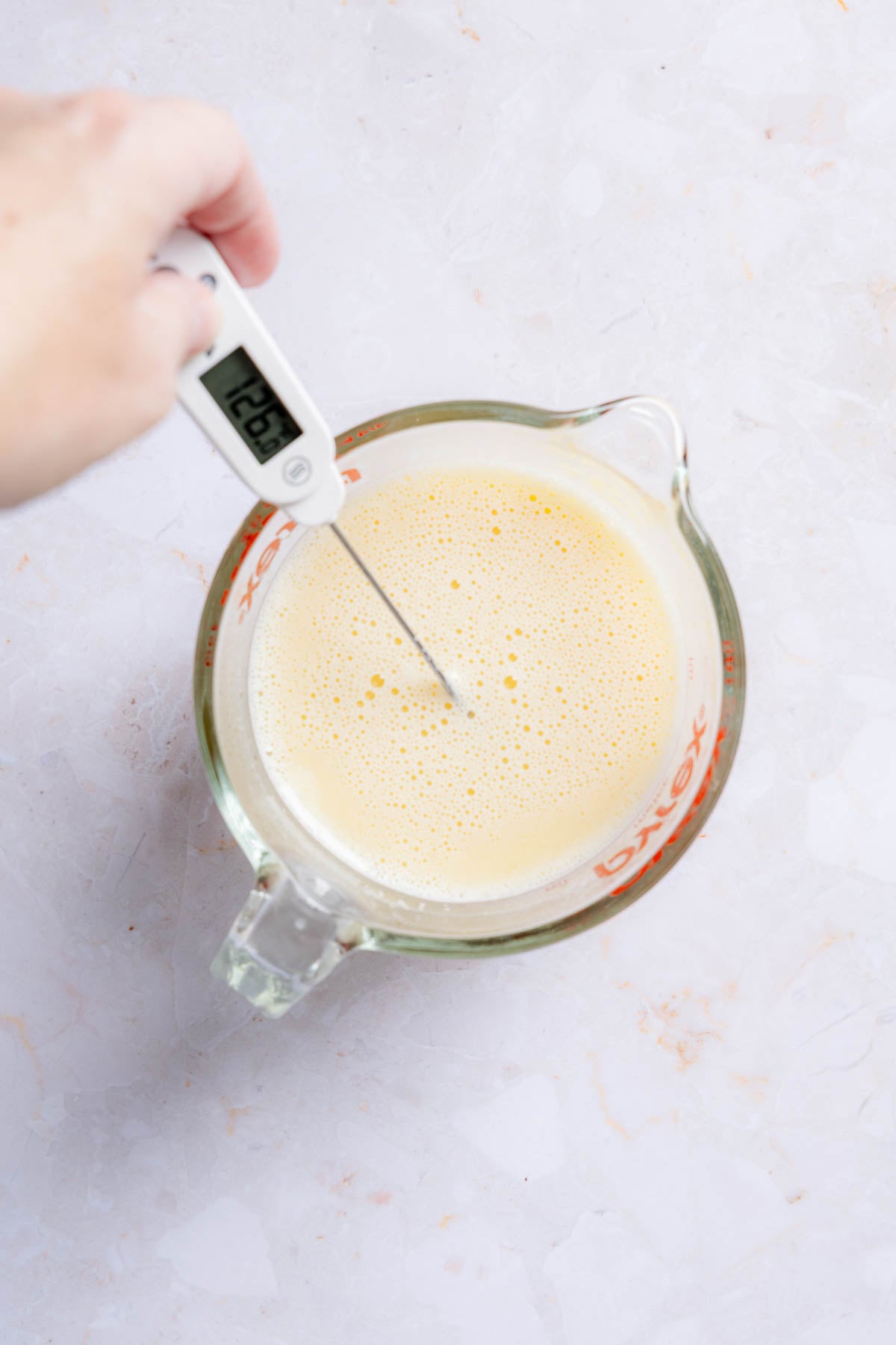 Checking temperature of whisked liquid ingredients in liquid measuring cup with digital thermometer.