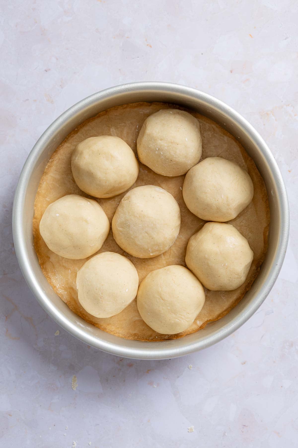 Eight dough balls arranged in round pan, before rising.
