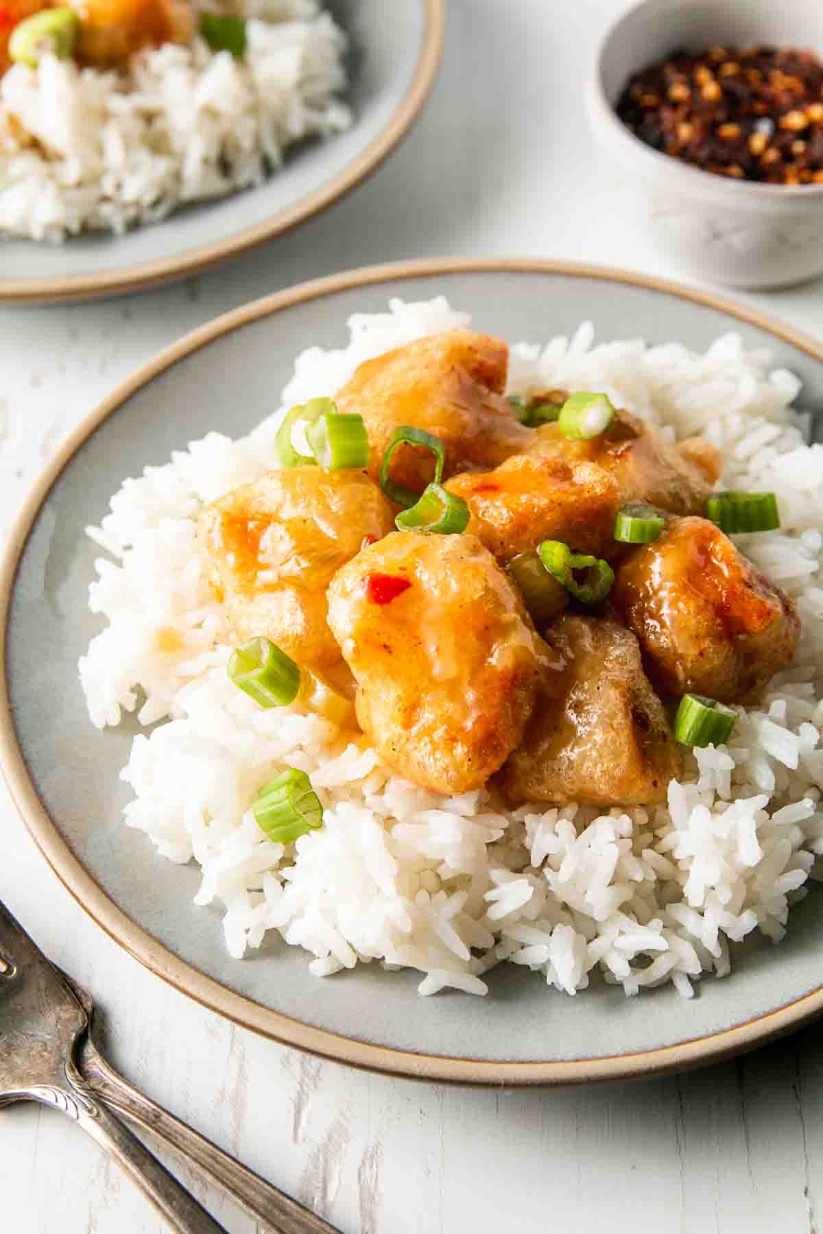 A bed of rice on a plate with pf Changs spicy chicken piled on top, sprinkled with green onions.