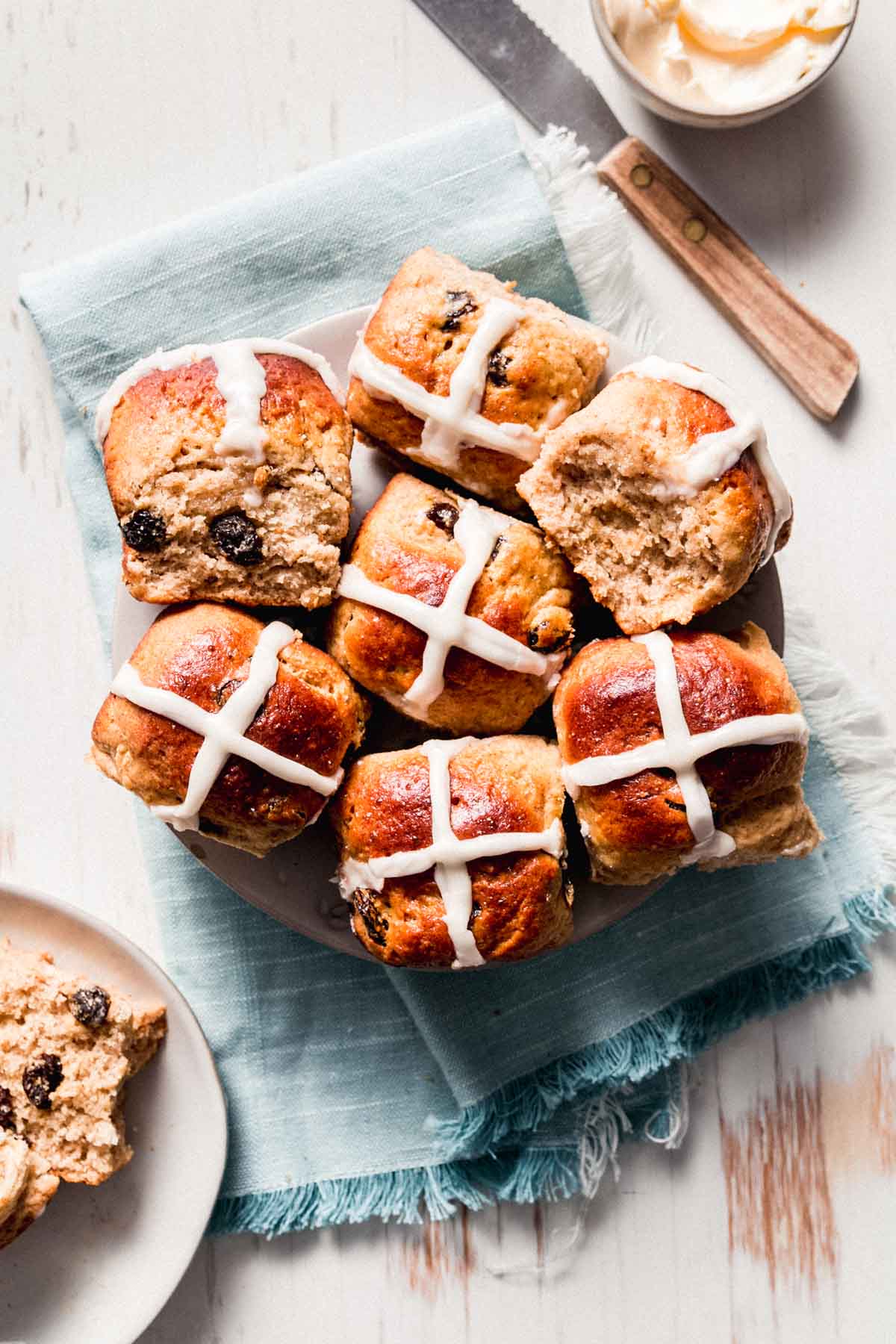A plate with gluten-free hot cross buns spilling over the edges. One split to the side.
