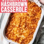 Golden brown hashbrown casserole held by hands on handles with white towel.