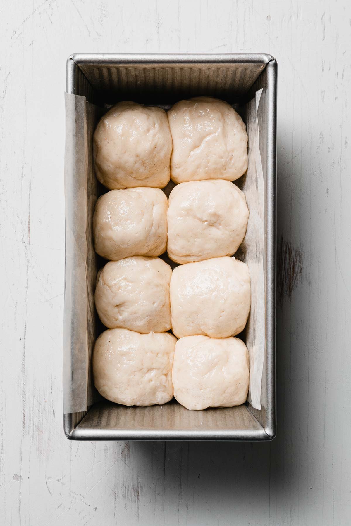 Eight shaped gluten-free roll dough balls placed snugly in a loaf pan, ready to rise.