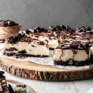 Gluten Free Oreo Cheesecake on a rustic wooden cake stand, sliced to show interior filled with cookies and cream.