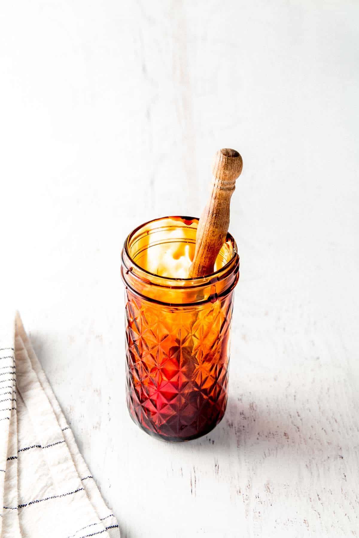 An empty quilted mason jar with leftover molasses on the sides. A wooden spoon resting in the jar.