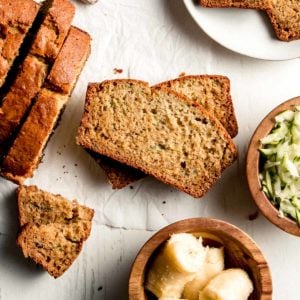 Gluten-free Zucchini Banana Bread sliced, laid on it's side, next to the rest of the loaf and a dish of zucchini and banana.