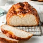 Braided gluten-free brioche loaf on wire rack, partially sliced to show interior texture.