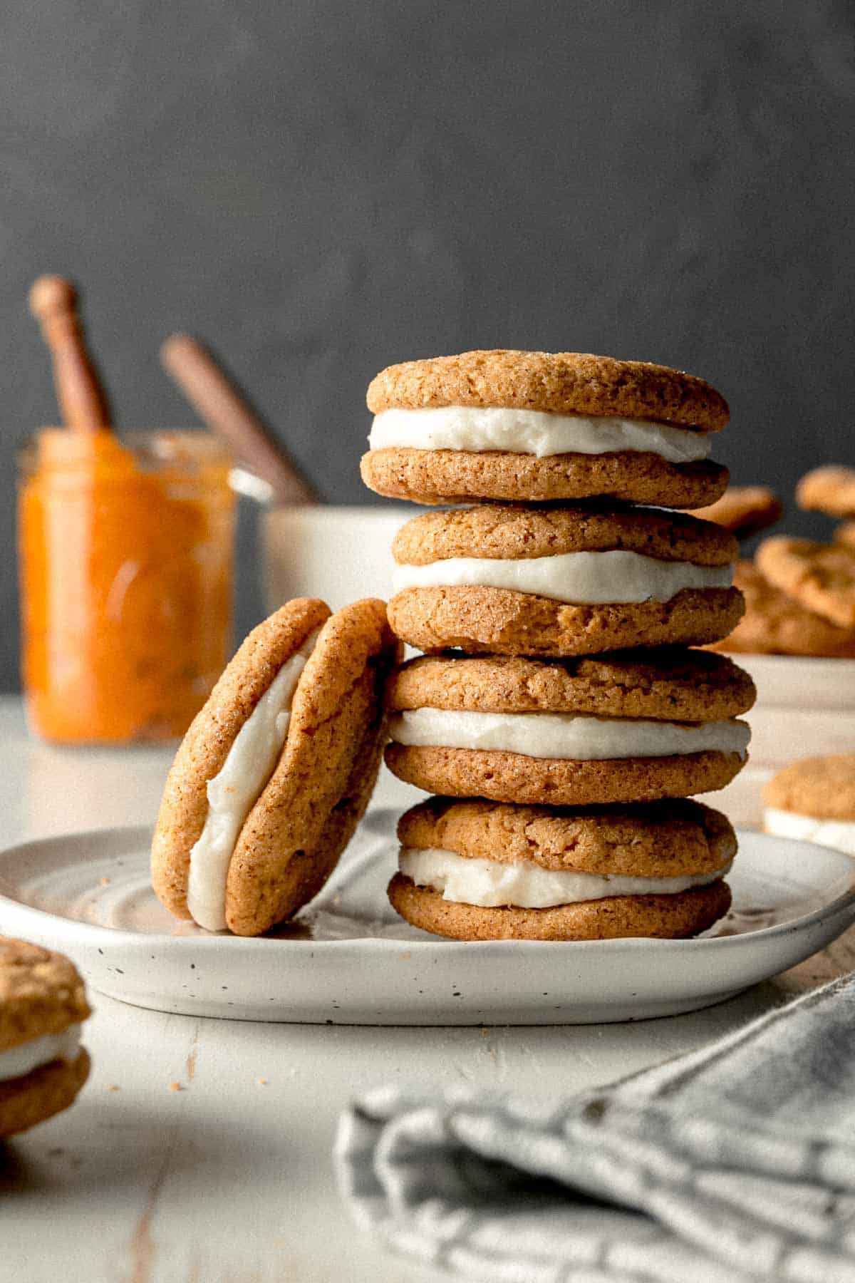 A stack of pumpkin cream pies, one cookie leaning against the stack. Pumpkin puree and a frosting bowl in the background.