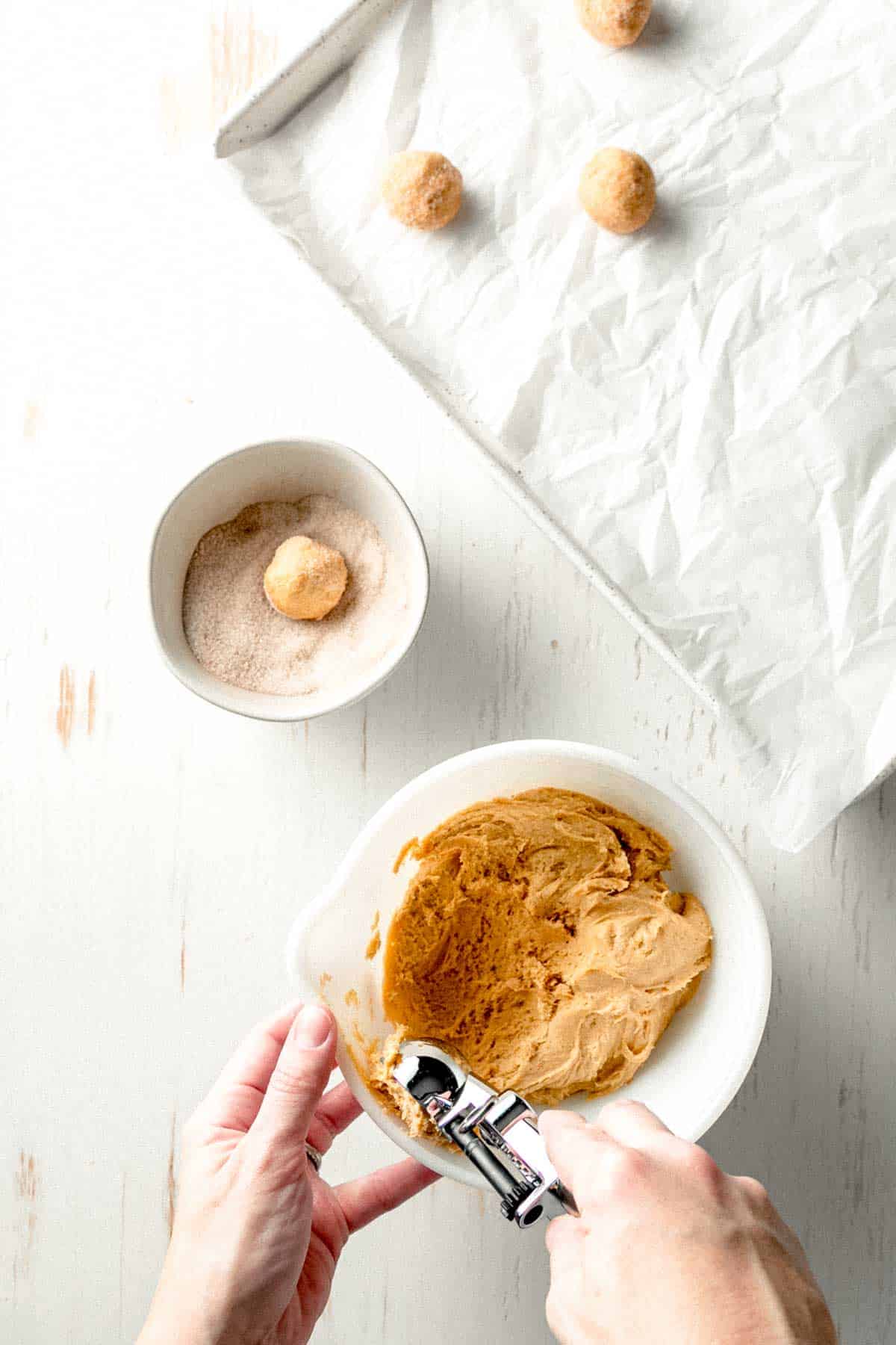 Scooping and rolling dough in cinnamon sugar and placing on parchment lined baking sheet.