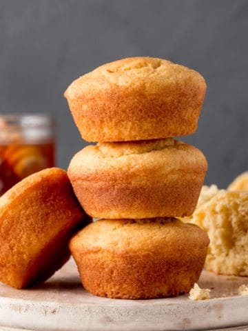 Three gluten-free jiffy style corbbread muffins stacked on a white wooden plate.