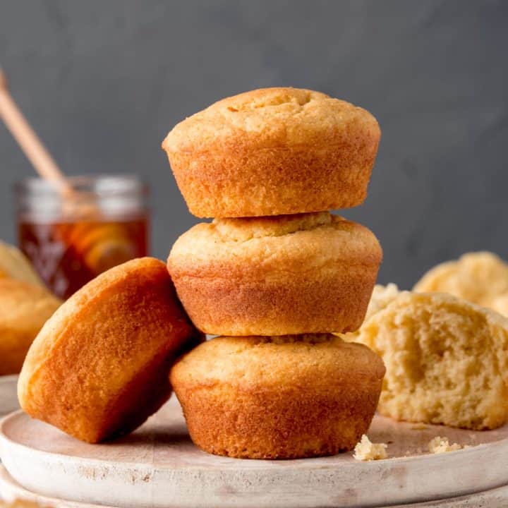 Three gluten-free jiffy style corbbread muffins stacked on a white wooden plate.