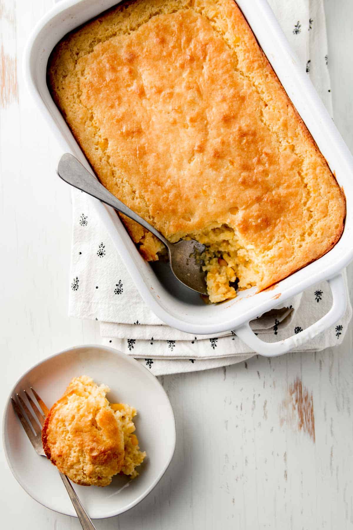 Gluten free cornbread casserole in a white baking dish with a scoop removed on a small plate.