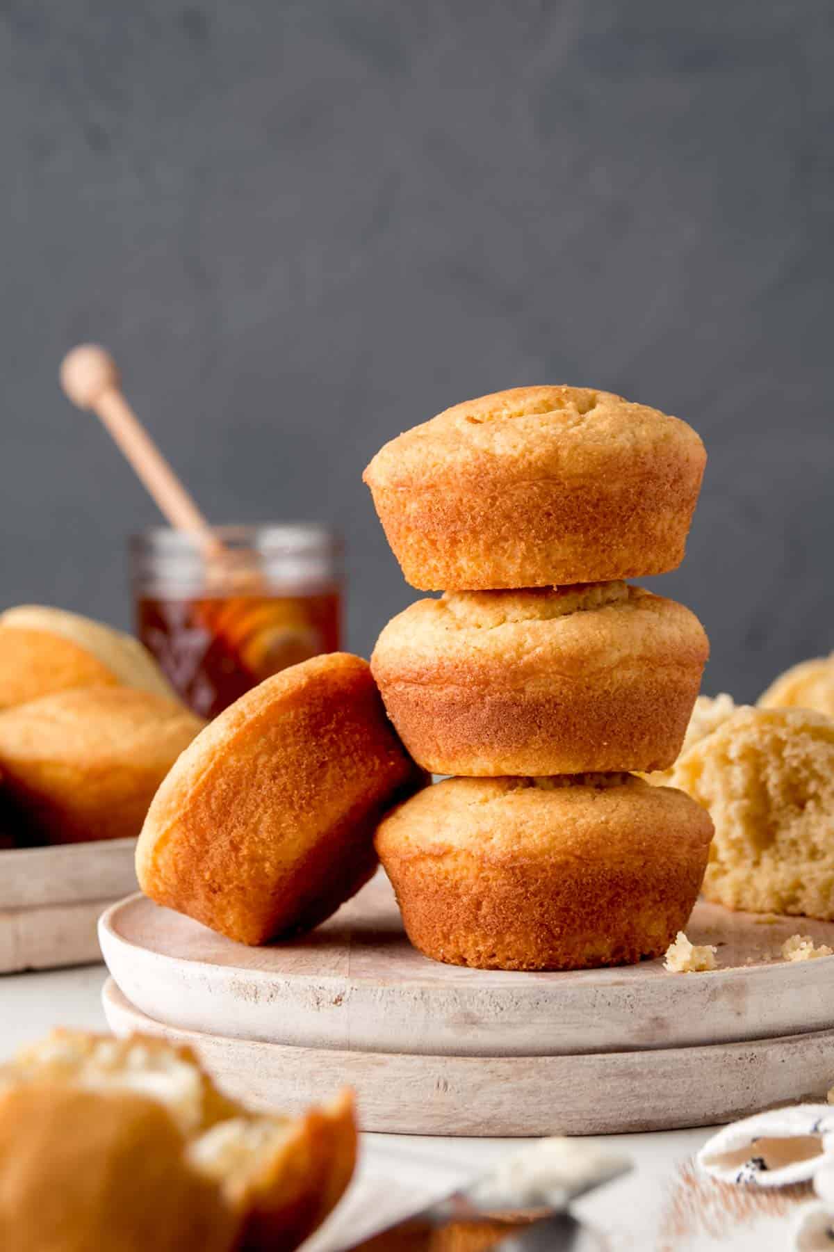 Three gluten-free jiffy style corbbread muffins stacked on a white wooden plate.