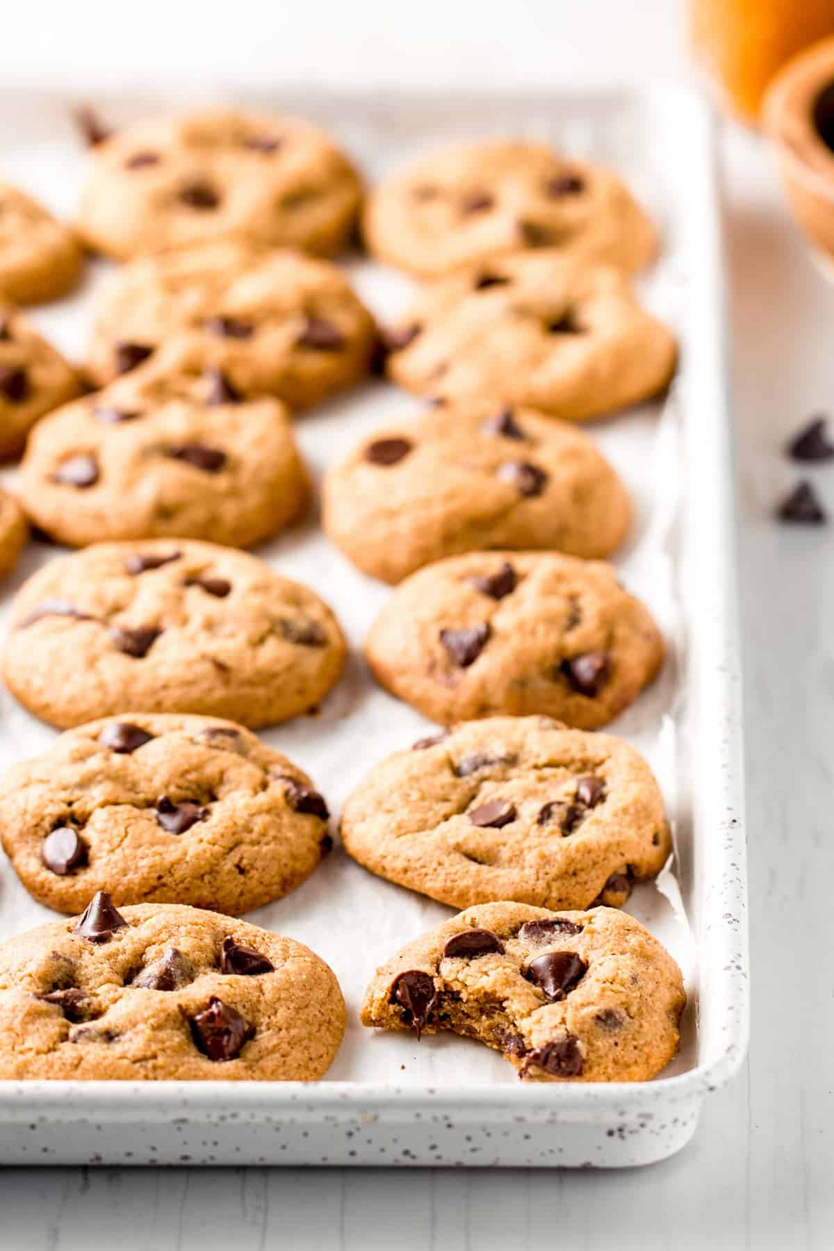 Gluten-free pumpkin chocolate chip cookies lined up on a white cookie sheet.