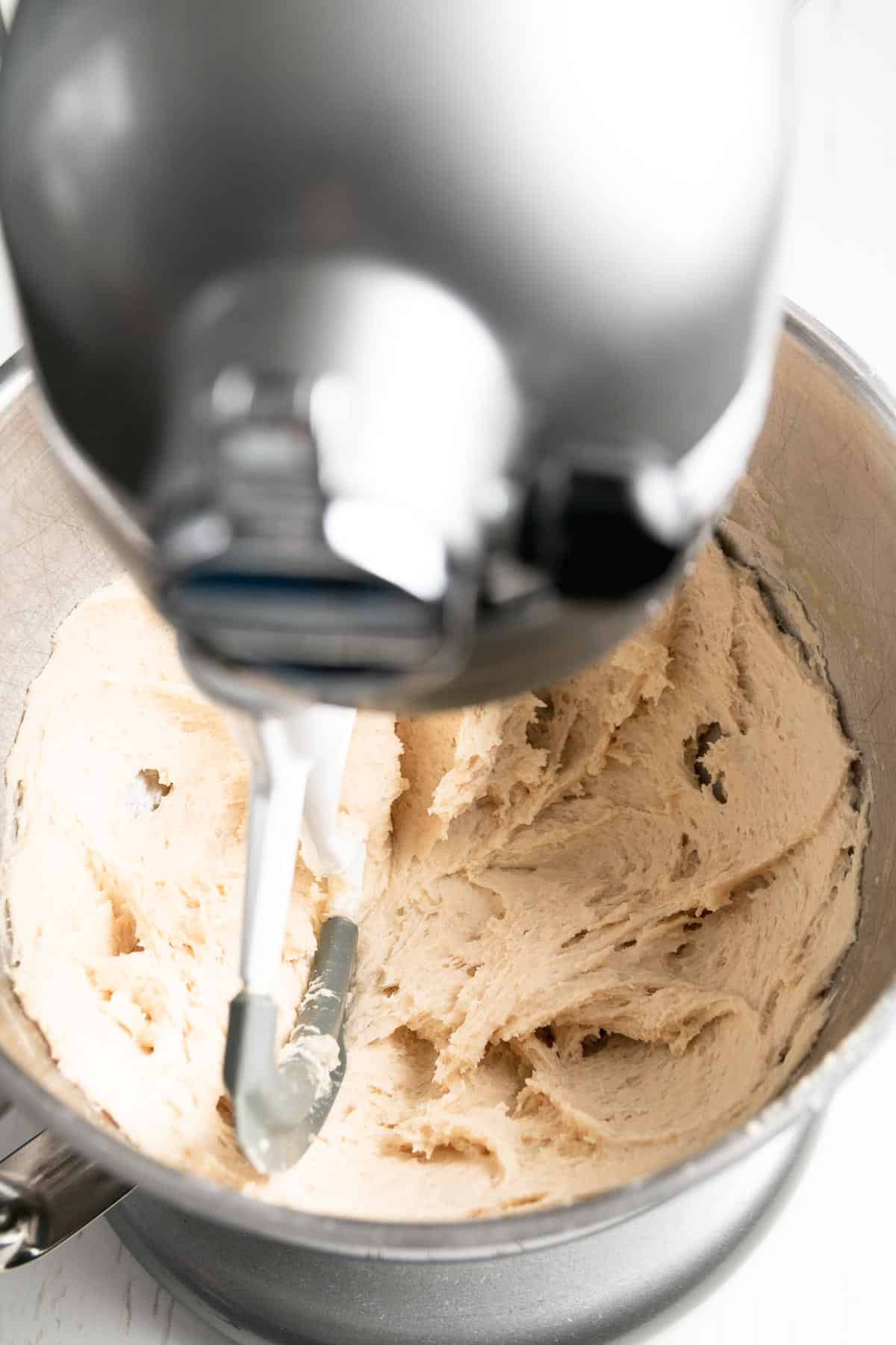Dough for gluten-free Hawaiian Rolls in bowl of stand mixer being mixed with paddle attachment.